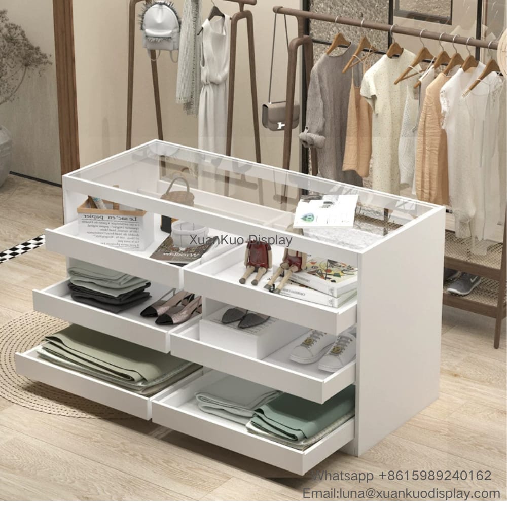 minimalist white clothing store display cabinet, transparent glass top, multiple pull-out divided drawers, multi-compartment storage for folded clothes, shoes and accessories, central display island for women fashion apparel boutique